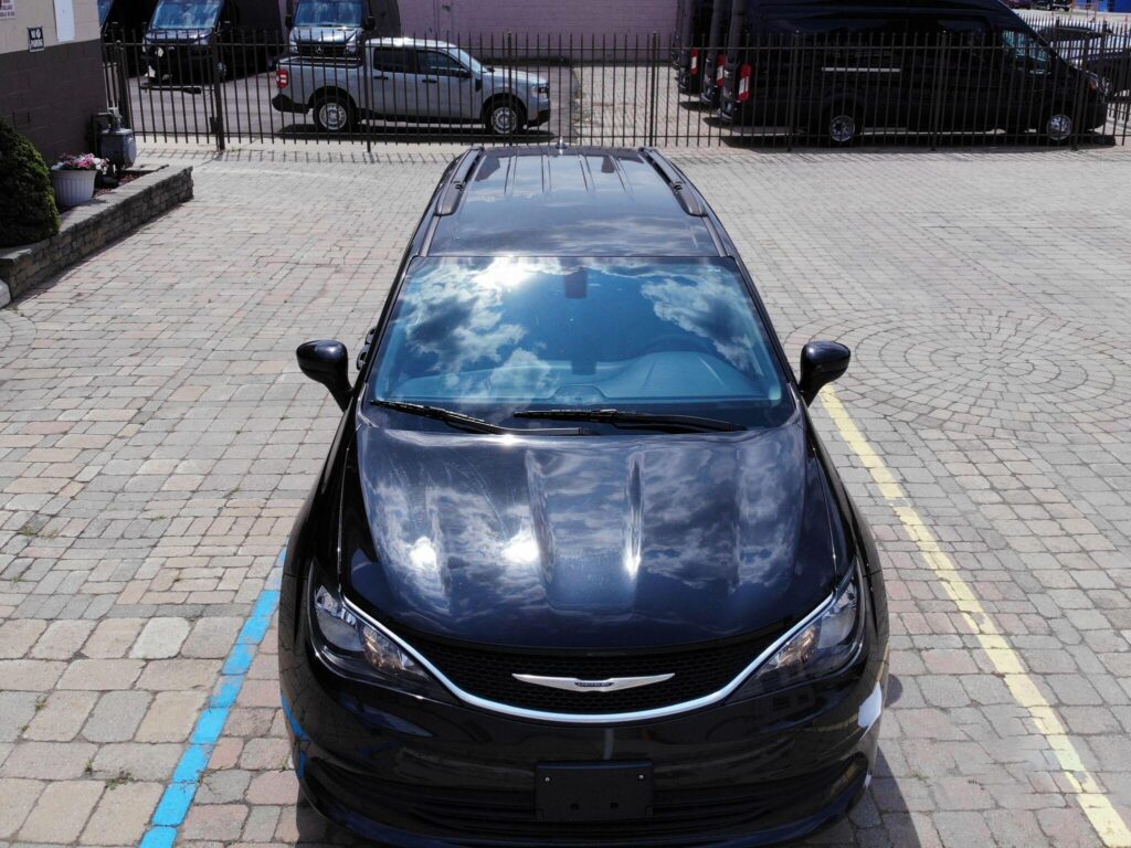  Top front view of a black car parked on a paved lot reflecting clouds on its hood and windshield.