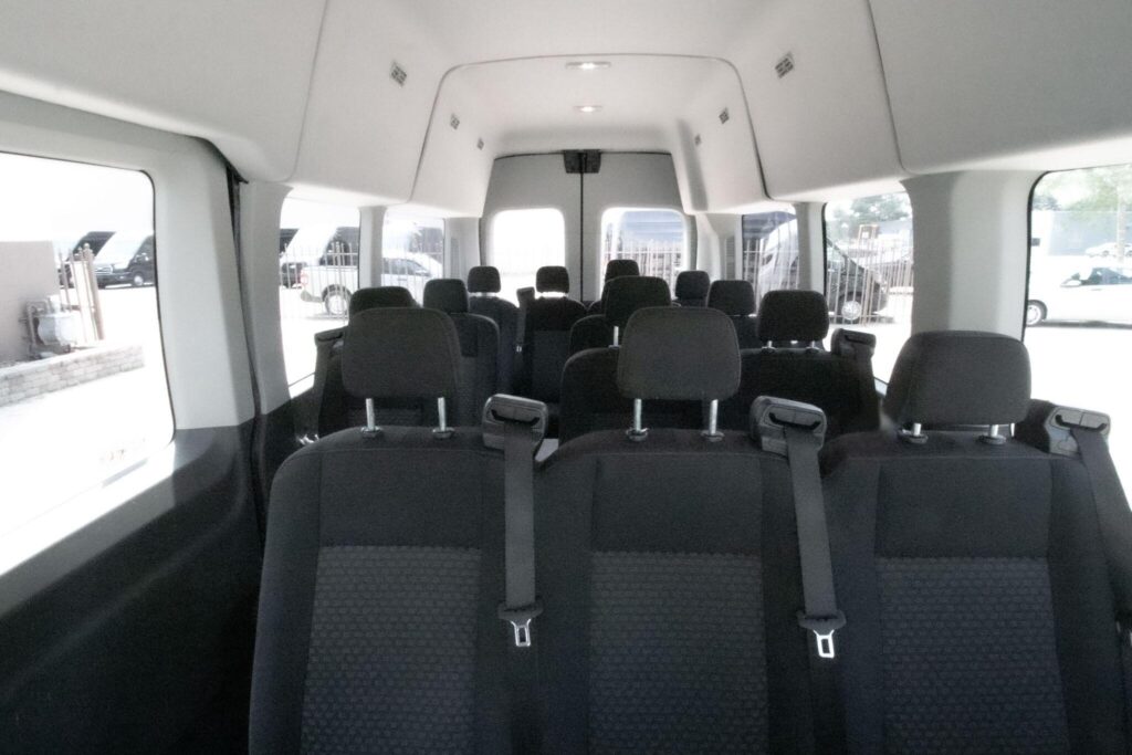 Interior view of a passenger van showing multiple rows of black seats with seatbelts.