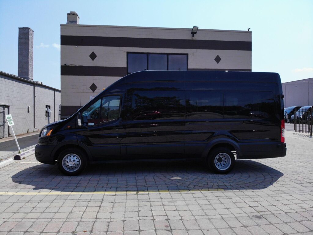 Black passenger van parked in a paved lot beside a building with a striped and diamond-patterned facade