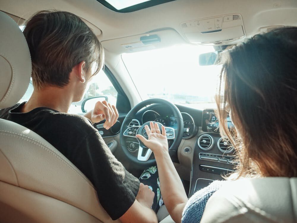 Two people sitting in the front seats of a car are having a conversation while parked or driving