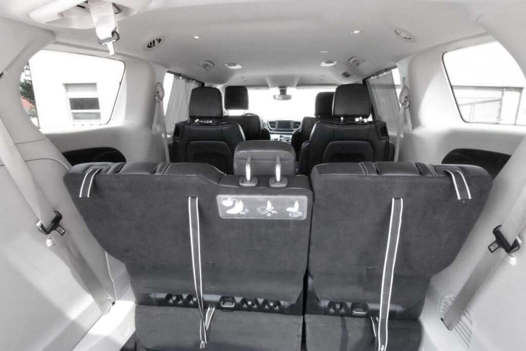 The image shows the interior of a passenger van or minivan, viewed from the back, featuring three rows of black seats