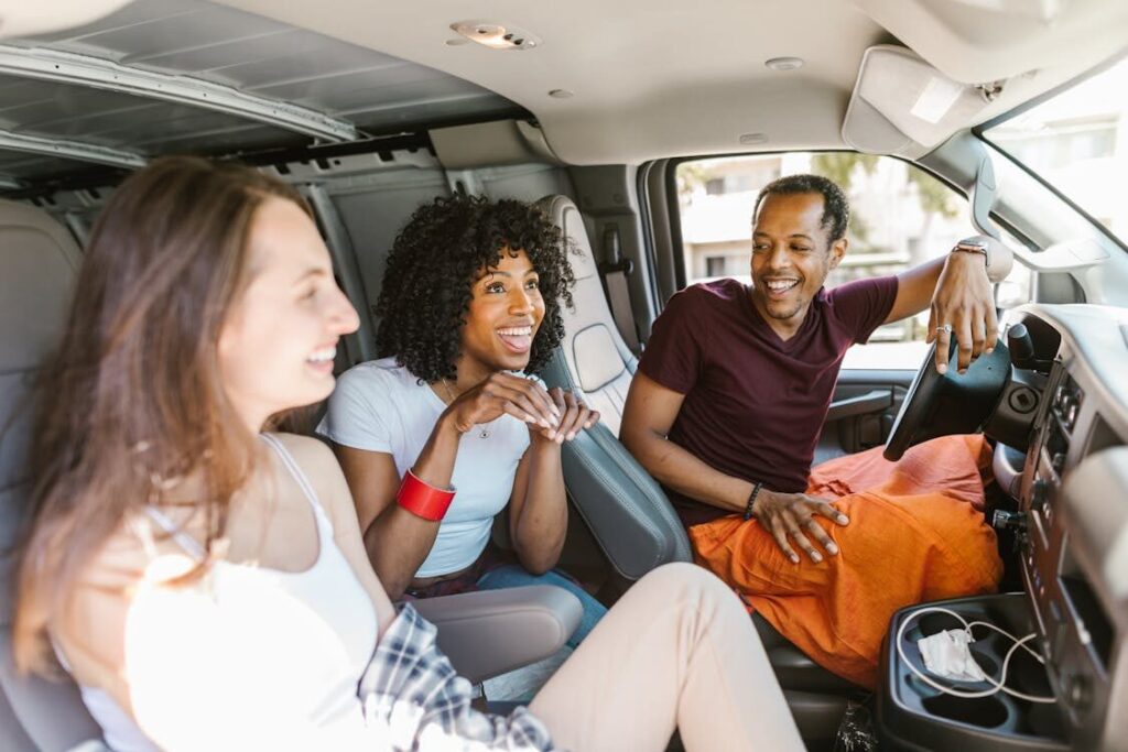 The image shows three people smiling and chatting inside a van, creating a relaxed and friendly atmosphere