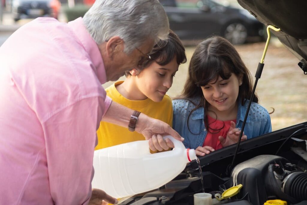 A grandfather is teaching his grandchildren how to pour fluid into an engine