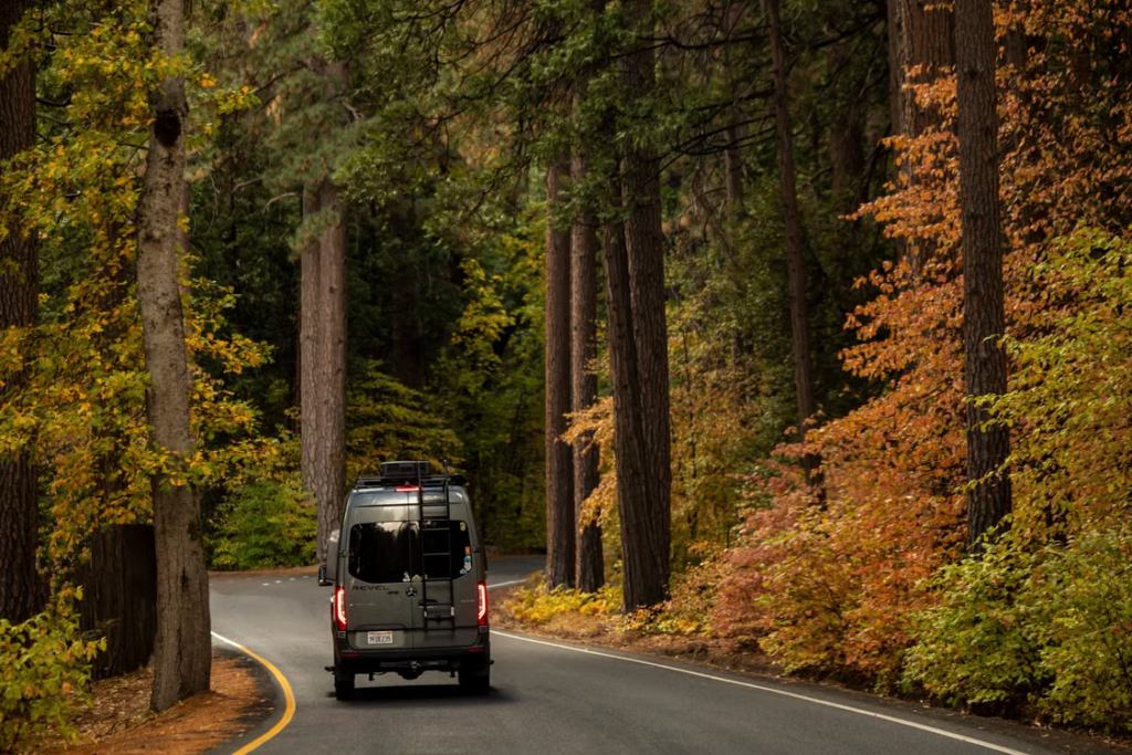A van travels down a winding road surrounded by vibrant autumn foliage